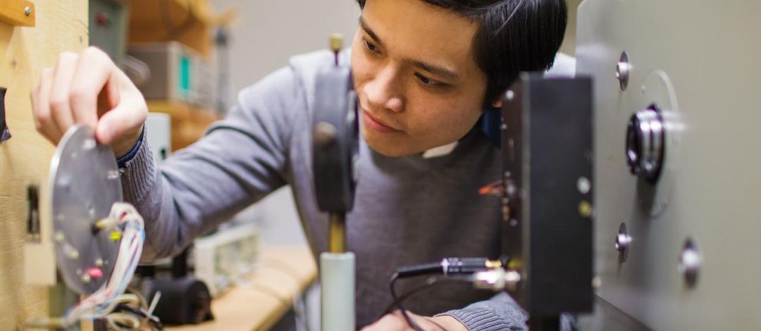 Foto: ein junger Mann, asiatischer Herkunft, experimentiert im Physiklabor