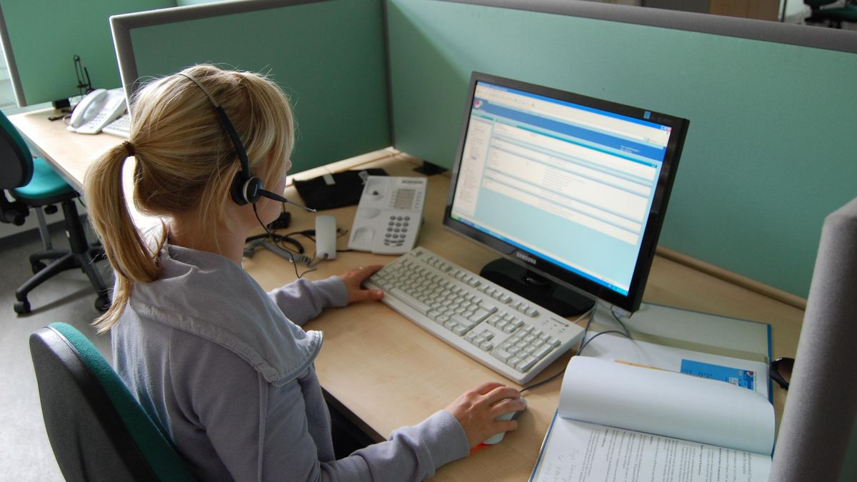 Eine junge Frau arbeitet am PC, auf dem Kopf hat sie ein Headset.