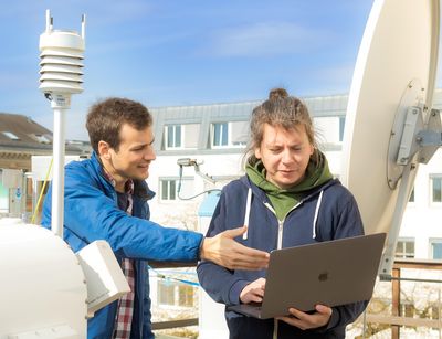Two young men stand on the roof of the institute behind the micro rain radar and look on a laptop. Photo: Swen Reichhold 