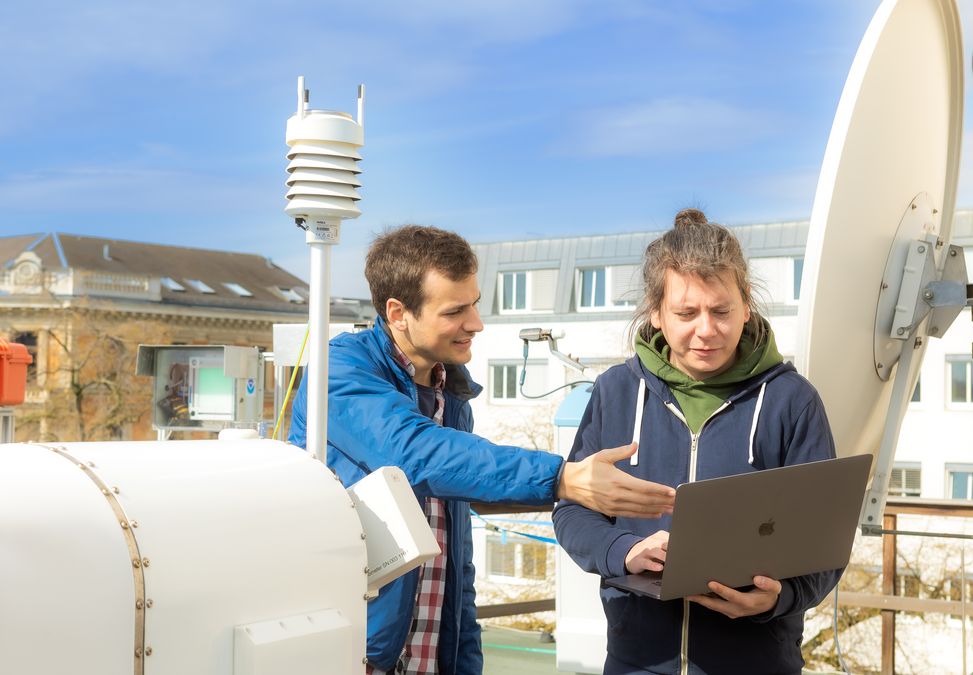 enlarge the image: Two young men stand on the roof of the institute behind the micro rain radar and look on a laptop. Photo: Swen Reichhold 