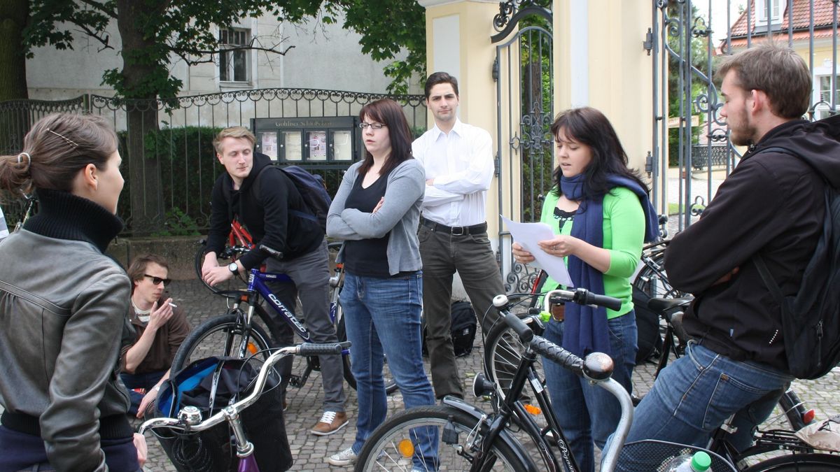 Eine Gruppe junger Menschen auf Rädern hört einer jungen Frau bei einem Vortrag zu.