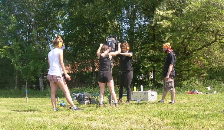Studierende und Mitarbeiterinnen des Instituts für Geographie führen während eines Feldpraktikums eine Rammkernsondierung auf einer Wiese bei Sonnenschein durch, Foto: C. Zielhofer