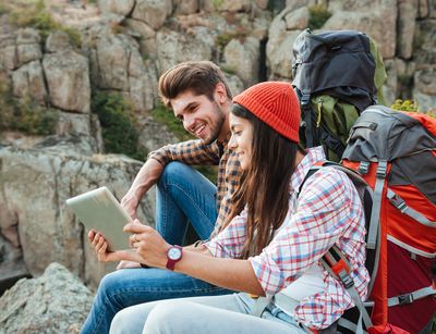 A man and a woman sit in the mountains looking at a tablet. Photo: Colourbox