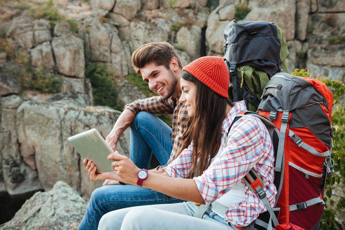 zur Vergrößerungsansicht des Bildes: Ein Mann und eine Frau sitzen in den Bergen und schauen auf ein Tablet. Foto: Colourbox