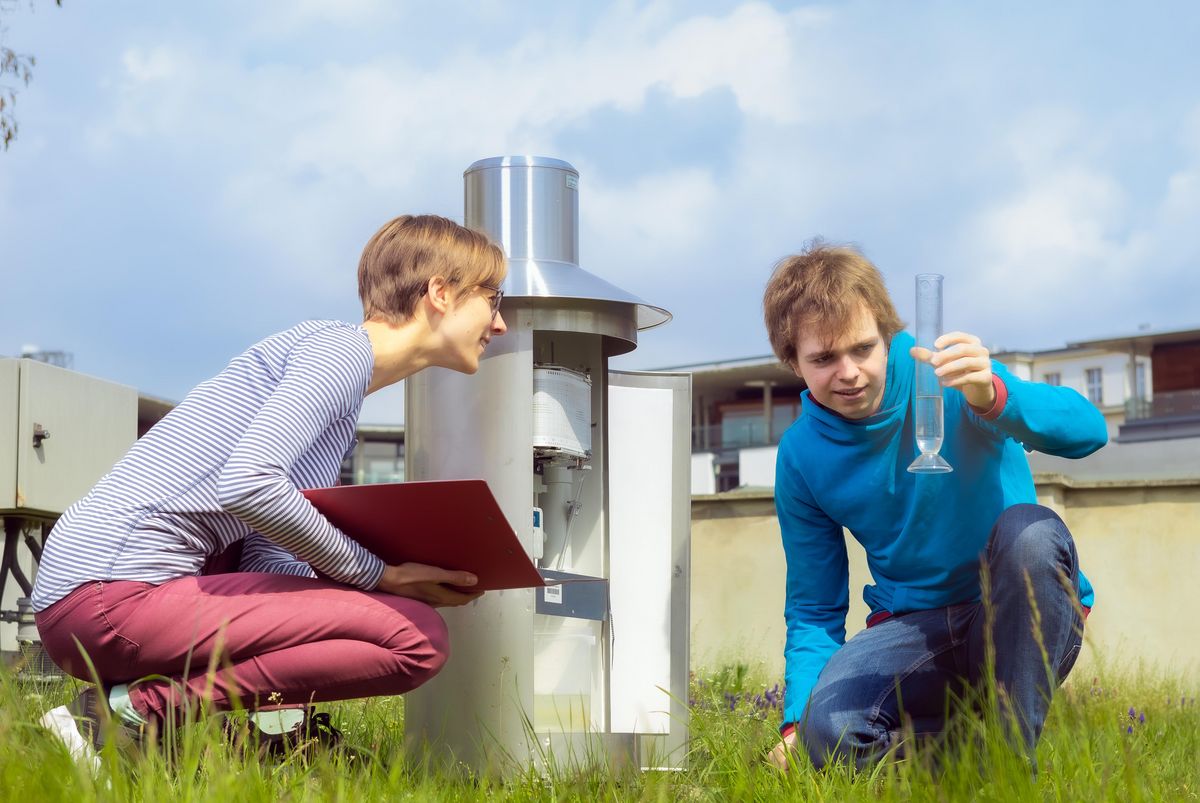 Zwei Studierden sitzen auf der Wetterwiese. Ein Studierender hät einen Glaszylinder hoch und eine Studierende liest ab. Foto. Swen Reichhold