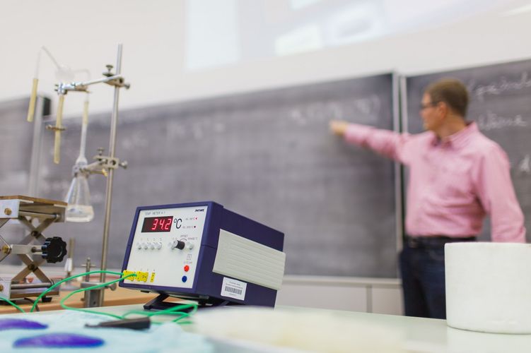 View of an experiment with different devices. In the background, the lecturer points to the full blackboard