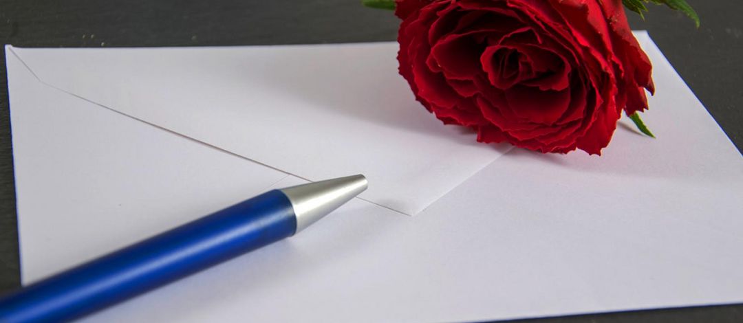 Briefumschlag, auf dem ein Kugelschreiber und eine Rose liegt