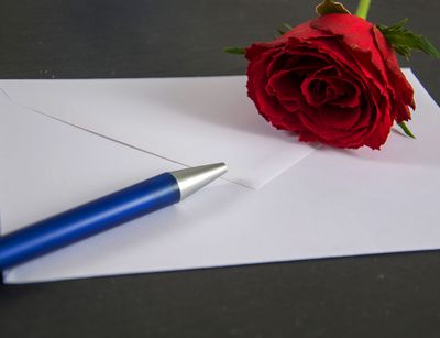 Briefumschlag, auf dem ein Kugelschreiber und eine Rose liegt